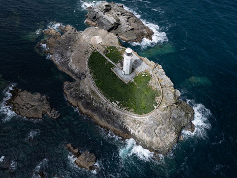 Aerial view of the white Godrevy Lighthouse situated on a rocky island with green grass and stone walls surrounded by the dark blue sea in Gwithian England United Kingdom. Aerial view of the white Godrevy Lighthouse situated on a rocky island with green grass and stone walls surrounded by the dark blue sea in Gwithian England United Kingdom.