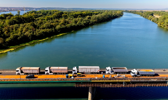 Aerial view of Smederevo bridge with a line of semi trucks crossing the Danube river surrounded by lush trees under a clear sky in Smederevo Podunavlje District Serbia.