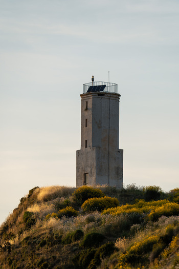 View of the historic Zvernec Lighthouse standing on a grassy hill with yellow wildflowers under a soft sky near Narta Lagoon in Zvernec Vlore County Albania.