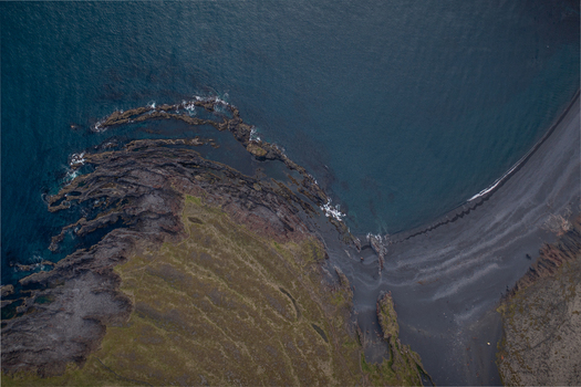 Aerial view of Djupalonssandur featuring dramatic black volcanic rock formations extending into the dark blue Atlantic Ocean along the rugged coastline of Iceland. Aerial view of Djupalonssandur featuring dramatic black volcanic rock formations extending into the dark blue Atlantic Ocean along the rugged coastline of Iceland.