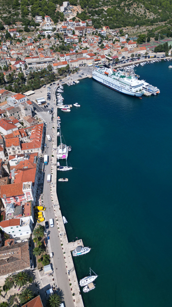 Aerial view of the harbor with a large ferry docked at the pier historic stone buildings with red roofs and boats along the waterfront in Vis Split Dalmatia County Croatia. Aerial view of the harbor with a large ferry docked at the pier historic stone buildings with red roofs and boats along the waterfront in Vis Split Dalmatia County Croatia.