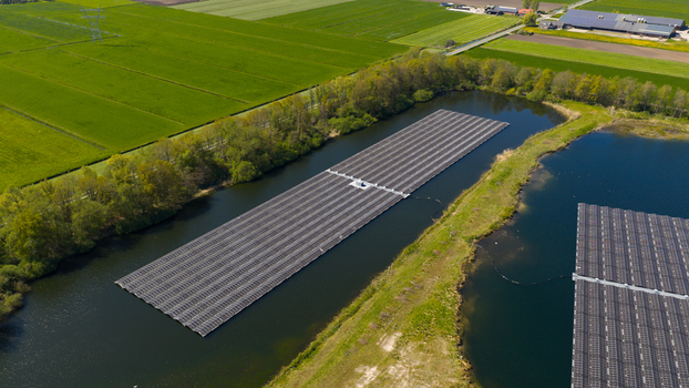 Aerial view of floating solar panels on a calm lake surrounded by lush green fields and trees under bright sunlight Zwolle Overijssel Netherlands. Aerial view of floating solar panels on a calm lake surrounded by lush green fields and trees under bright sunlight Zwolle Overijssel Netherlands.