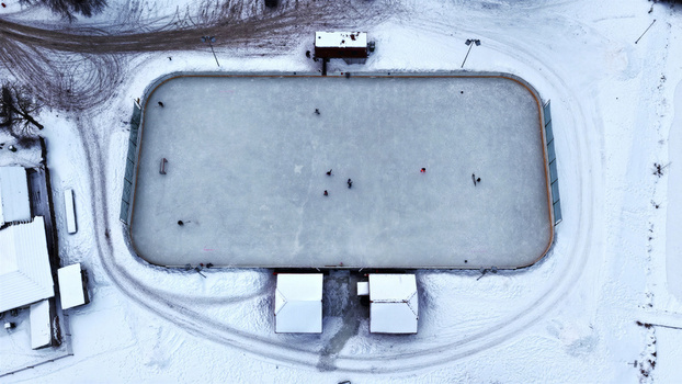 Aerial view of an outdoor ice rink surrounded by snow covered ground with people skating on the ice in Latvija. Aerial view of an outdoor ice rink surrounded by snow covered ground with people skating on the ice in Latvija.