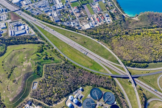 Aerial view of a highway interchange slicing through verdant fields and industrial zones a modern artery contrasting with the natural landscape Sausheim Grand Est France.