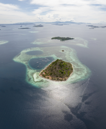 Aerial view of Pulau Kukusan island surrounded by turquoise coral reefs and deep blue sea in Komodo East Nusa Tenggara Indonesia. Aerial view of Pulau Kukusan island surrounded by turquoise coral reefs and deep blue sea in Komodo East Nusa Tenggara Indonesia.