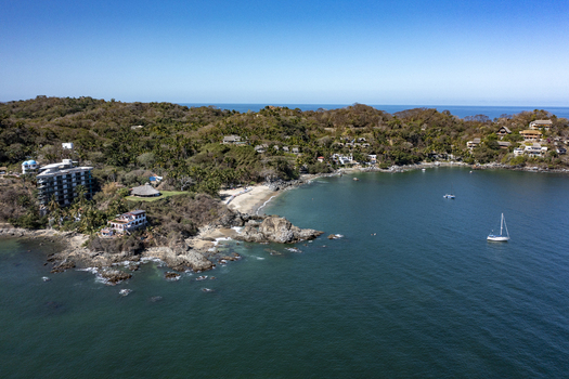 Aerial view of the coastal landscape featuring a sandy beach rocky cliffs lush tropical vegetation hillside villas and a sailboat in the bay Sayulita Nayarit Mexico. Aerial view of the coastal landscape featuring a sandy beach rocky cliffs lush tropical vegetation hillside villas and a sailboat in the bay Sayulita Nayarit Mexico.