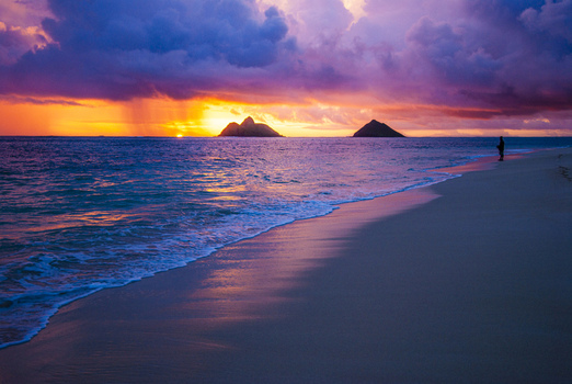 View of Lanikai Beach at sunset with vibrant purple and orange clouds over the ocean and the Mokulua Islands in the distance in Kailua Hawaii United States.