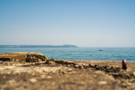View of the calm sea and horizon with a small boat framed by a weathered stone structure in the foreground under a clear blue sky in Charlestown Cornwall United Kingdom. View of the calm sea and horizon with a small boat framed by a weathered stone structure in the foreground under a clear blue sky in Charlestown Cornwall United Kingdom.