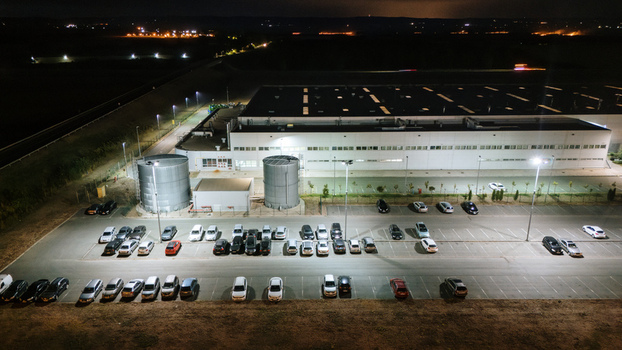 Aerial view of an industrial facility at night with a large warehouse two metal water tanks and a parking lot filled with cars under bright floodlights in Sremska Mitrovica Vojvodina Serbia. Aerial view of an industrial facility at night with a large warehouse two metal water tanks and a parking lot filled with cars under bright floodlights in Sremska Mitrovica Vojvodina Serbia.