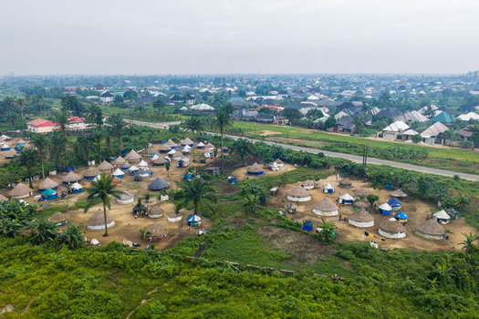 Aerial view of a rural settlement with traditional round huts thatched roofs and palm trees situated near a modern urban landscape in Port Harcourt Rivers State Nigeria. Aerial view of a rural settlement with traditional round huts thatched roofs and palm trees situated near a modern urban landscape in Port Harcourt Rivers State Nigeria.
