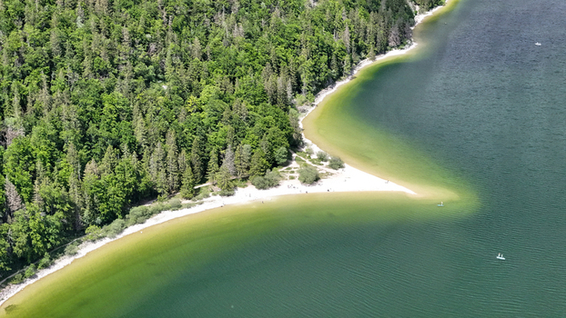Aerial view of the meeting of emerald waters and sandy shorelines fringed by the verdant forest of Lac de Joux Le Lieu Vaud Switzerland.