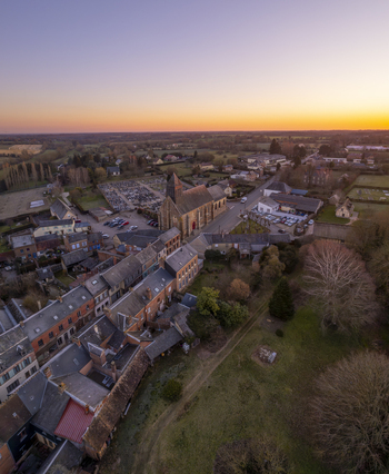 Aerial view of the village of Sap en Auge featuring a historic church surrounding stone houses a cemetery and green fields under a sunset sky in Sap en Auge Normandy France. Aerial view of the village of Sap en Auge featuring a historic church surrounding stone houses a cemetery and green fields under a sunset sky in Sap en Auge Normandy France.
