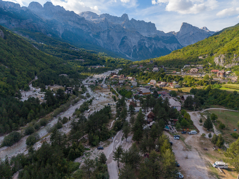 Aerial view of the village of Theth nestled in the Accursed Mountains with a rocky riverbed lush green forests and traditional houses in Theth Shkoder County Albania. Aerial view of the village of Theth nestled in the Accursed Mountains with a rocky riverbed lush green forests and traditional houses in Theth Shkoder County Albania.