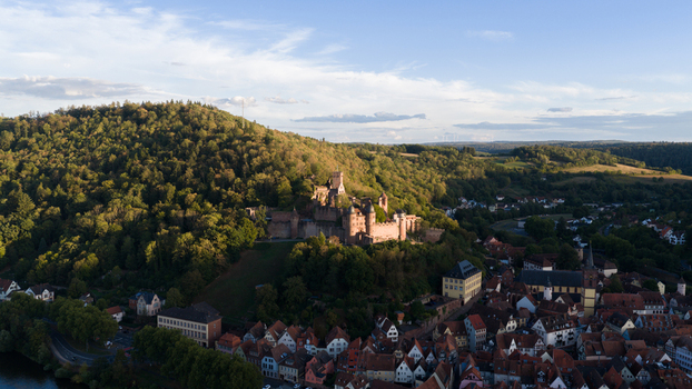 Aerial view of Wertheim Castle perched on a hill overlooking the historic town with dense forest red tiled rooftops and warm golden hour light in Wertheim Baden Wurttemberg Germany. Aerial view of Wertheim Castle perched on a hill overlooking the historic town with dense forest red tiled rooftops and warm golden hour light in Wertheim Baden Wurttemberg Germany.