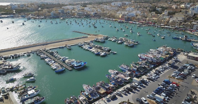 Aerial view of the colorful traditional luzzu fishing boats docked in the harbor of Marsaxlokk with the town buildings and clear blue water in the background in Marsaxlokk Malta Malta. Aerial view of the colorful traditional luzzu fishing boats docked in the harbor of Marsaxlokk with the town buildings and clear blue water in the background in Marsaxlokk Malta Malta.
