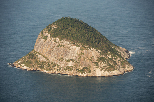 Aerial view of the rocky island of Ilha Rasa rising from the deep blue Atlantic Ocean with steep granite cliffs and lush green vegetation in Rio de Janeiro Rio de Janeiro Brazil. Aerial view of the rocky island of Ilha Rasa rising from the deep blue Atlantic Ocean with steep granite cliffs and lush green vegetation in Rio de Janeiro Rio de Janeiro Brazil.