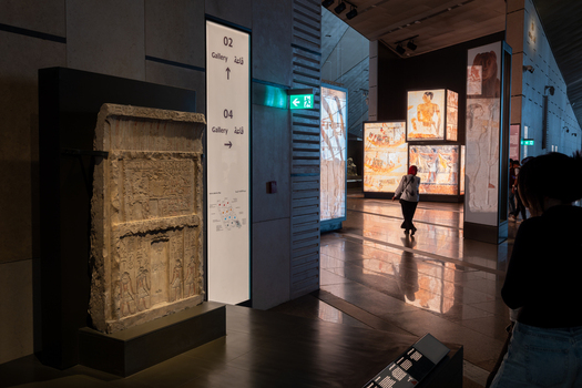 Giza Egypt 16 May 2026 View of the Grand Egyptian Museum interior featuring an ancient stone stela and illuminated displays with visitors walking through the gallery.