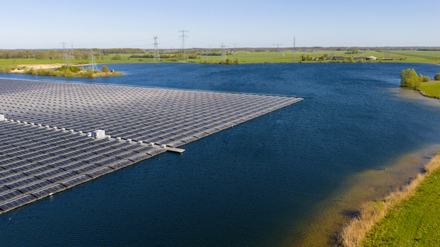 Aerial view of a large floating solar farm on a calm lake surrounded by green fields and power lines under a clear sky Zwolle Overijssel Netherlands. Aerial view of a large floating solar farm on a calm lake surrounded by green fields and power lines under a clear sky Zwolle Overijssel Netherlands.