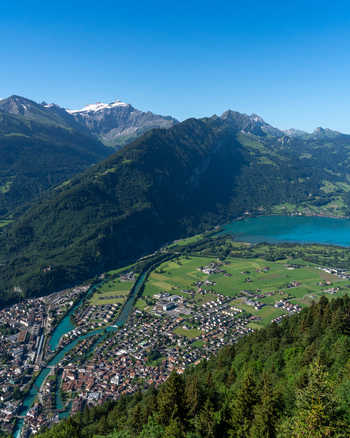 View of Harder Kulm overlooking the town of Unterseen the Aare river and Lake Thun nestled among the Swiss Alps under a clear blue sky. Unterseen Canton of Bern Switzerland.