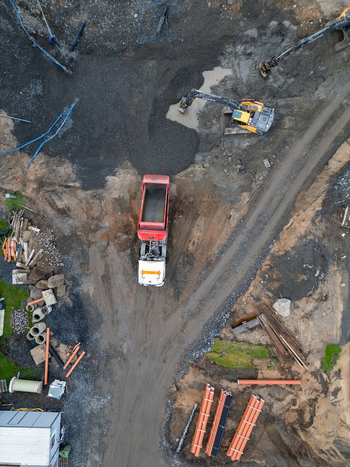 Oulu Finland 18 September 2026 Aerial view of construction site at waterfront with an excavator and a dump truck operating among pipes and materials. Oulu Finland 18 September 2026 Aerial view of construction site at waterfront with an excavator and a dump truck operating among pipes and materials.