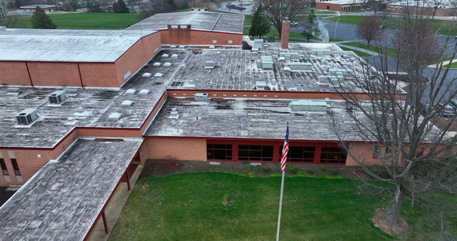 Aerial view of the Derry Township school building featuring a large flat roof with HVAC units red brick walls and an American flag flying in the front yard in Hershey Pennsylvania United States.