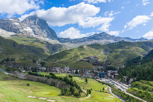Aerial view of the mountain village of Breuil Cervinia nestled in the Alps with the Matterhorn peak green meadows and a golf course in Breuil Cervinia Aosta Valley Italy. Aerial view of the mountain village of Breuil Cervinia nestled in the Alps with the Matterhorn peak green meadows and a golf course in Breuil Cervinia Aosta Valley Italy.