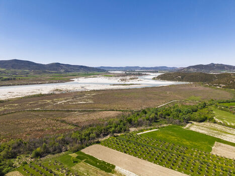 Aerial view of the Shkumbin riverbed with wide gravel banks surrounded by agricultural fields orchards and rolling hills in Lushnje Fier County Albania. Aerial view of the Shkumbin riverbed with wide gravel banks surrounded by agricultural fields orchards and rolling hills in Lushnje Fier County Albania.
