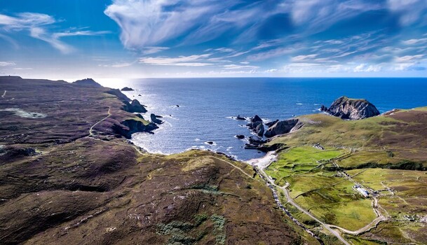 Aerial view of the rugged coastline at An Port featuring dramatic cliffs green fields and the Atlantic Ocean under a bright blue sky in Ardara County Donegal Ireland.