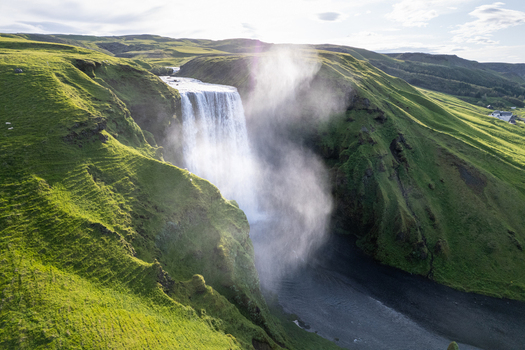 Aerial view of Skogafoss waterfall cascading down lush green cliffs with mist rising over the river in Rangarthing eystra Iceland.