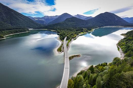 Aerial view of a serene lake reflecting the sky bisected by a long winding bridge connecting forested shores Sylvensteinspeicher Bavaria Germany. Aerial view of a serene lake reflecting the sky bisected by a long winding bridge connecting forested shores Sylvensteinspeicher Bavaria Germany.