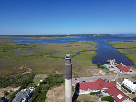 Aerial view of Oak Island Lighthouse standing near the marshlands and coastal buildings in Caswell Beach North Carolina United States.