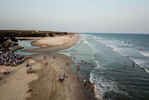 Aerial view of a sandy beach with people relaxing under umbrellas gentle waves rolling onto the shore and a calm ocean meeting the coastline in Ghana. Aerial view of a sandy beach with people relaxing under umbrellas gentle waves rolling onto the shore and a calm ocean meeting the coastline in Ghana.