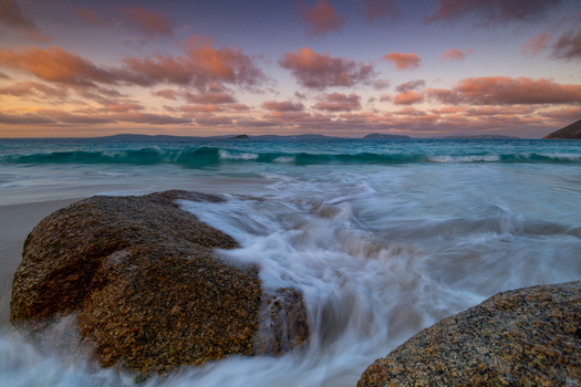 View of Misery Beach with granite boulders gentle waves washing over the sand and a colorful sunset sky over the Southern Ocean in Torndirrup Western Australia Australia. View of Misery Beach with granite boulders gentle waves washing over the sand and a colorful sunset sky over the Southern Ocean in Torndirrup Western Australia Australia.