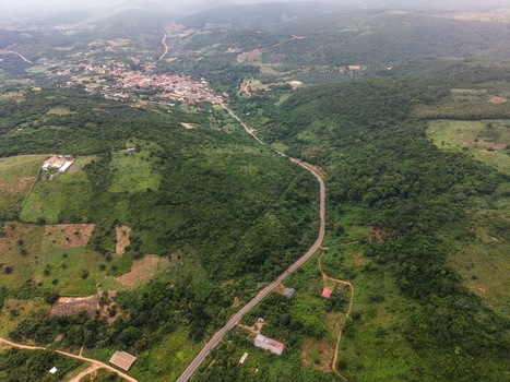 Aerial view of a winding road cutting through lush green hills and forests with a small town visible in the distance in Ghana. Aerial view of a winding road cutting through lush green hills and forests with a small town visible in the distance in Ghana.