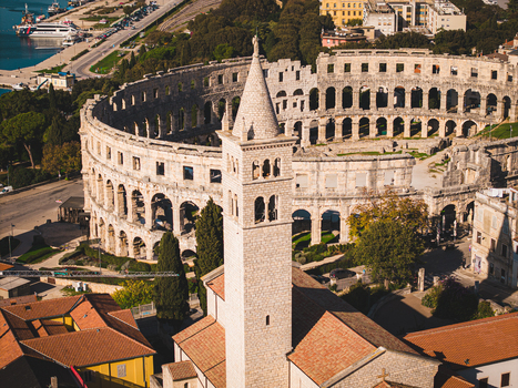 Aerial view of the ancient Roman amphitheater stands majestically beside a towering church steeple a blend of history and faith Pula Istria County Croatia. Aerial view of the ancient Roman amphitheater stands majestically beside a towering church steeple a blend of history and faith Pula Istria County Croatia.