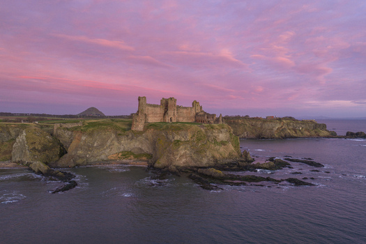 Aerial view of Tantallon Castle on a rocky cliff overlooking the sea under a vibrant pink sunset sky North Berwick Scotland United Kingdom.