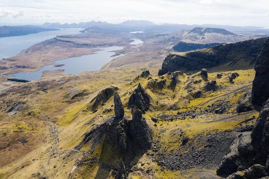 Aerial view of The Storr rock formations on the Isle of Skye with rugged green slopes rocky cliffs and distant lochs in Portree Scotland United Kingdom. Aerial view of The Storr rock formations on the Isle of Skye with rugged green slopes rocky cliffs and distant lochs in Portree Scotland United Kingdom.