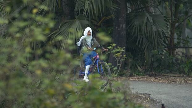 View of a schoolgirl riding a bicycle in a rural area Bangladesh. View of a schoolgirl riding a bicycle in a rural area Bangladesh.