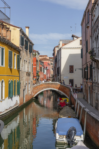 View of a narrow canal lined with historic colorful buildings a small brick arch bridge and a boat moored in the water under a clear blue sky in Venice Veneto Italy. View of a narrow canal lined with historic colorful buildings a small brick arch bridge and a boat moored in the water under a clear blue sky in Venice Veneto Italy.