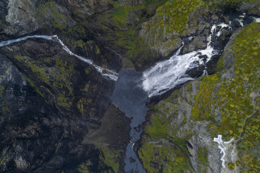 Aerial view of Voringfossen waterfall cascading down steep rocky cliffs into a deep canyon with lush green moss and a viewing platform Eidfjord Municipality Vestland Norway.