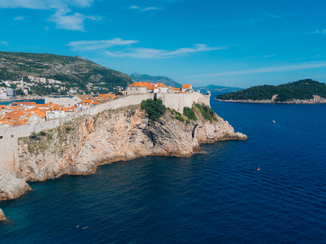 View of the historic stone walls and red tiled roofs of the Old Town on a rocky cliff overlooking the blue Adriatic Sea in Dubrovnik Dubrovnik Neretva County Croatia. View of the historic stone walls and red tiled roofs of the Old Town on a rocky cliff overlooking the blue Adriatic Sea in Dubrovnik Dubrovnik Neretva County Croatia.