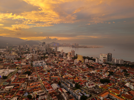 George Town Malaysia 22 September 2026 Aerial view of George Town cityscape at sunset with historic rooftops modern skyscrapers and the coastline under a golden sky.