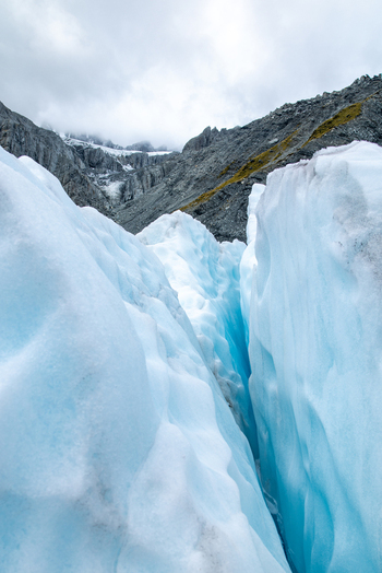 View of a deep blue crevasse cutting through the stark white ice of Franz Josef Glacier under a cloudy sky Franz Josef Glacier West Coast Region New Zealand. View of a deep blue crevasse cutting through the stark white ice of Franz Josef Glacier under a cloudy sky Franz Josef Glacier West Coast Region New Zealand.