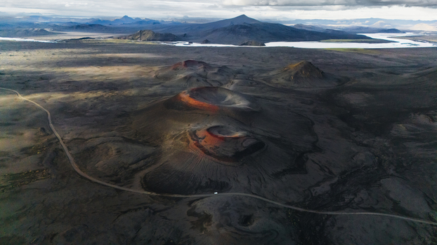 Aerial view of volcanic craters with dark lava fields red tinted rims and a winding dirt road through the rugged landscape of Iceland. Aerial view of volcanic craters with dark lava fields red tinted rims and a winding dirt road through the rugged landscape of Iceland.