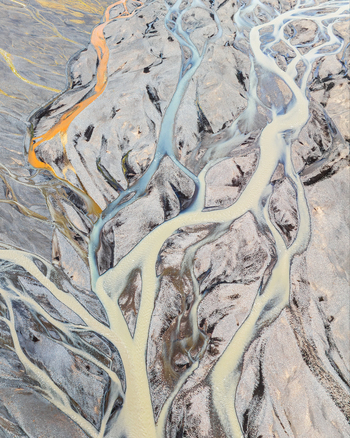 Aerial view of braided glacial river channels with sediment rich water flowing through a dark volcanic landscape in Iceland. Aerial view of braided glacial river channels with sediment rich water flowing through a dark volcanic landscape in Iceland.