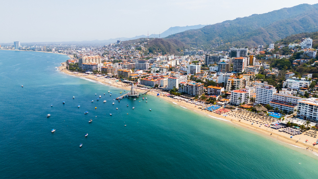 Aerial view of the vibrant blend of turquoise waters meeting golden sands framed by the bustling cityscape and verdant mountains Puerto Vallarta Jalisco Mexico.