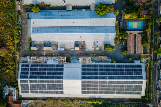 Aerial view of a large industrial factory building featuring extensive rooftop solar panel arrays surrounded by green vegetation and nearby structures in Semarang Regency Central Java Indonesia. Aerial view of a large industrial factory building featuring extensive rooftop solar panel arrays surrounded by green vegetation and nearby structures in Semarang Regency Central Java Indonesia.