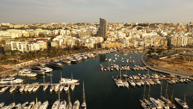 Aerial view of a marina filled with numerous yachts and boats surrounded by urban buildings and coastal infrastructure in Malta. Aerial view of a marina filled with numerous yachts and boats surrounded by urban buildings and coastal infrastructure in Malta.