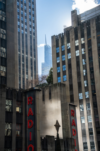 Manhattan United States 03 December 2025 View of Radio City Music Hall with its striking neon against the aged facade framed by modern skyscrapers reaching for the pale blue sky.