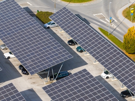 Aerial view of solar panel carports covering a parking lot with parked cars and a nearby road Slovenia.